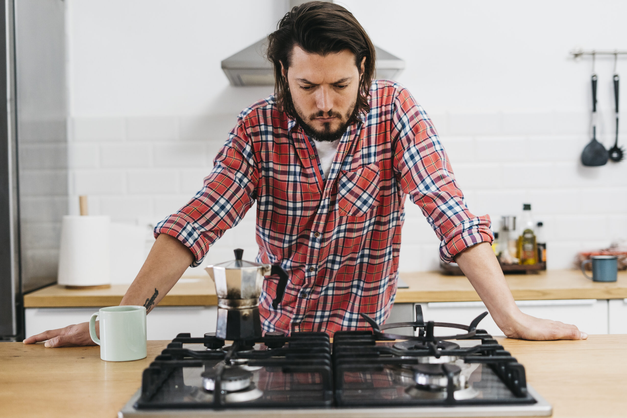 Serious young man leaning on and staring at gas oven.